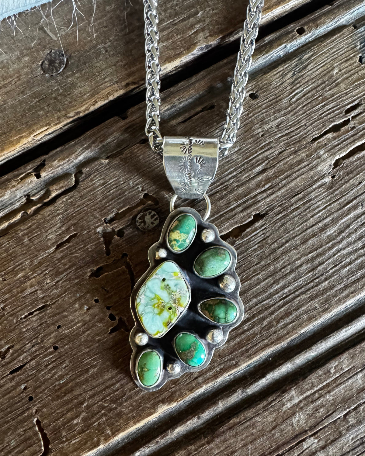 A silver-toned paw print pendant necklace with green turquoise-like stones and a white central stone, displayed on a rustic wooden surface.