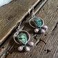 Pair of earrings with green and pink stones on a wooden surface