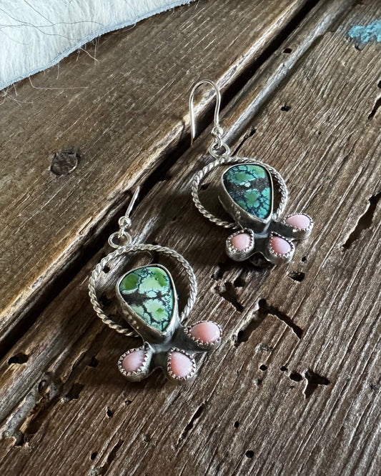 Pair of earrings with green and pink stones on a wooden surface