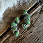 Green stone earrings on a wooden surface with white fabric
