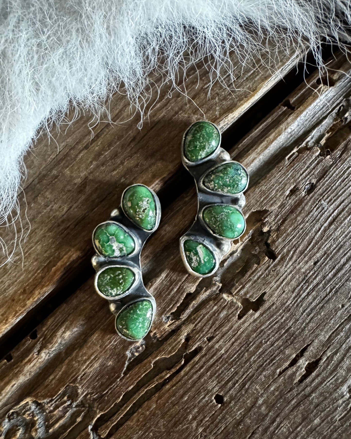 Green stone earrings on a wooden surface with white fabric