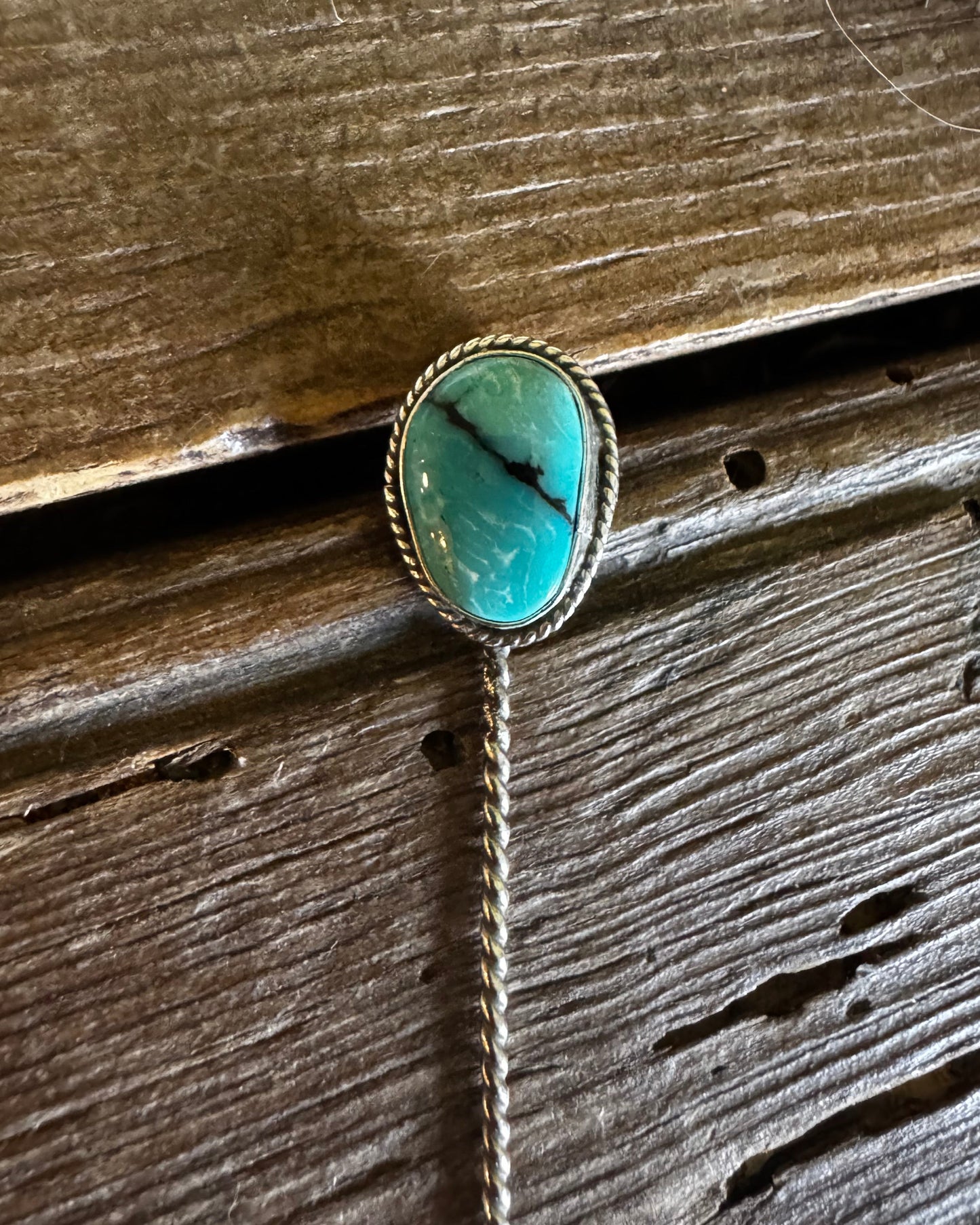 Turquoise stone pendant on a chain against a wooden background