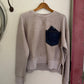 tan sweater with a patch on a hanger against a white wall.