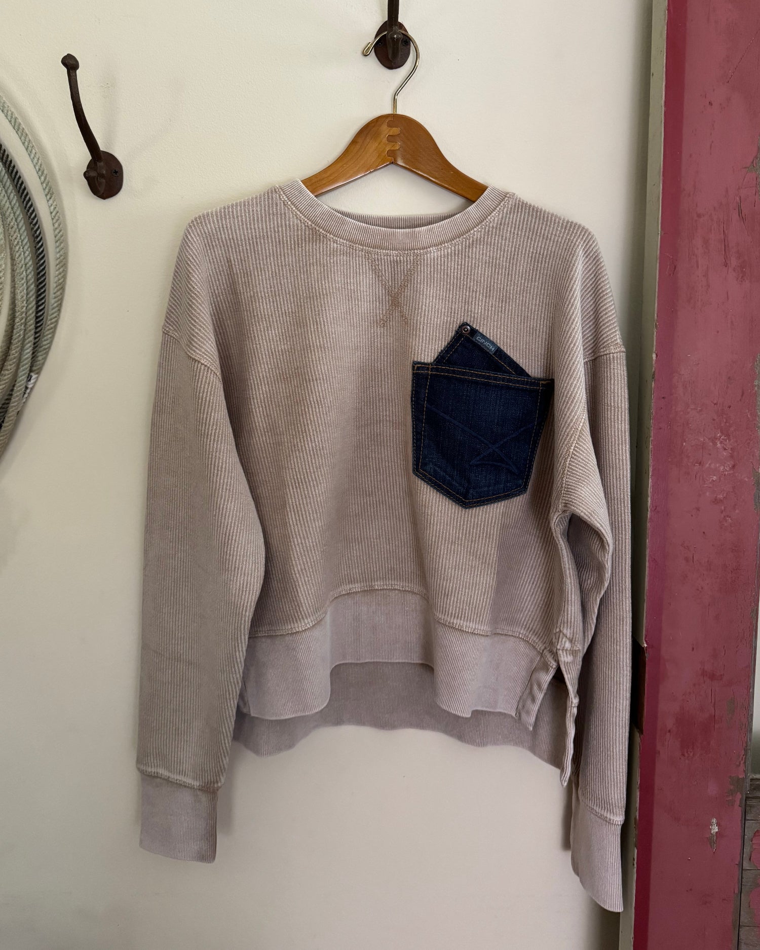 tan sweater with a patch on a hanger against a white wall.