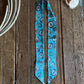 Blue patterned ribbon scarf on a wooden surface with cowhide leather and rope.