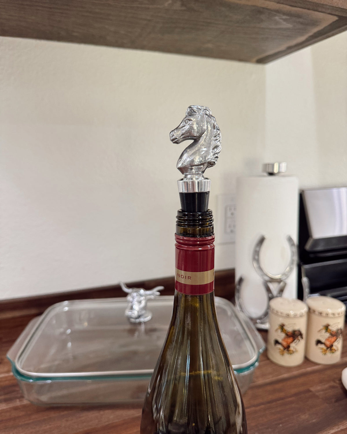 Wine bottle with a silver horse-shaped stopper on a wooden surface.