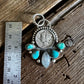 Silver pendant with turquoise stones on a wooden surface next to a ruler for scale.