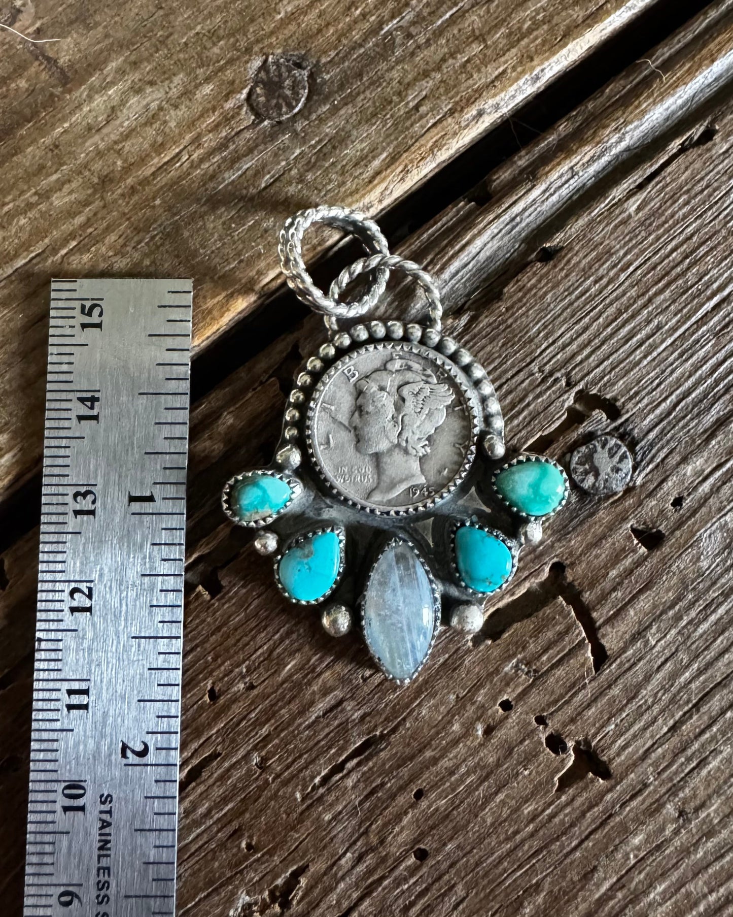 Silver pendant with turquoise stones on a wooden surface next to a ruler for scale.