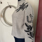 Gray sweater with black floral and horseshoe designs on a mannequin against a neutral background.
