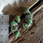Two silver earrings with green gemstones on a wooden surface with a ruler for scale.