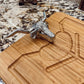 A silver bull head cheese knife resting on a rectangular bamboo cutting board with a geometric design, set on a speckled granite countertop.