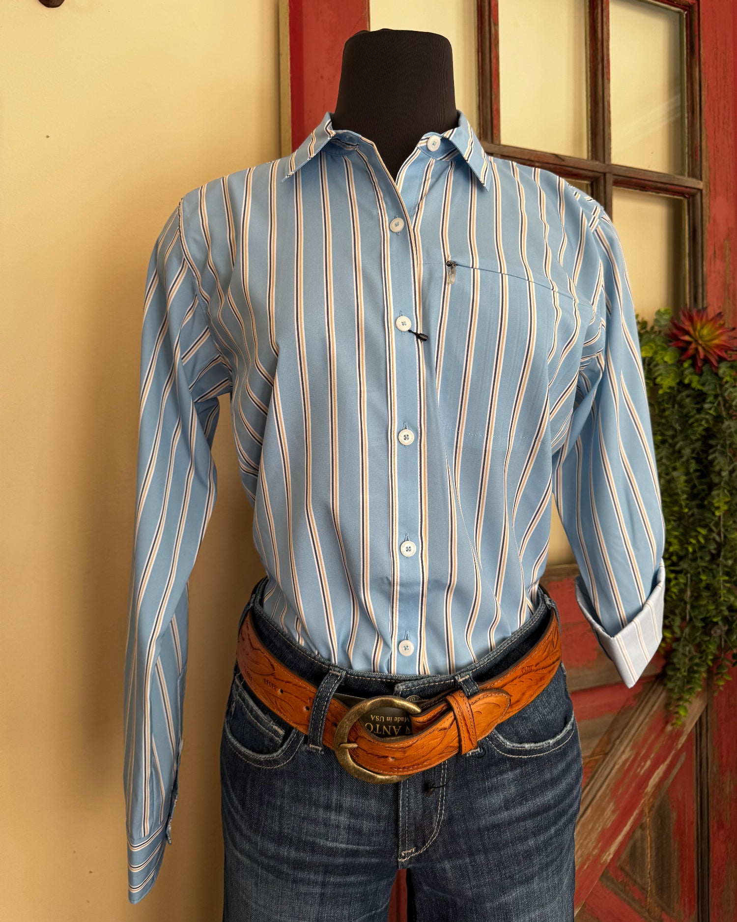 Person wearing a blue striped shirt and jeans with a brown belt, standing indoors.