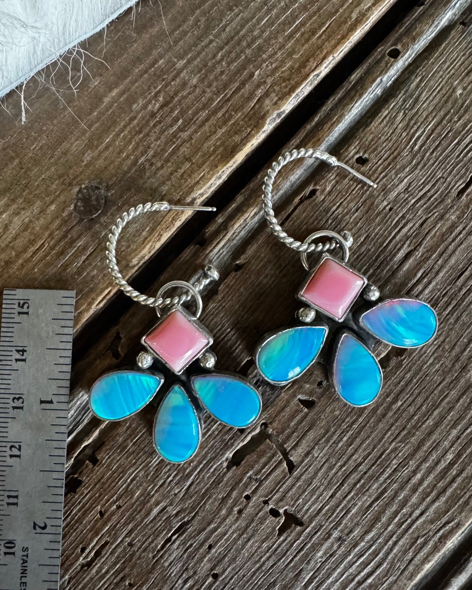 Butterfly-shaped earrings with pink and blue wings on a wooden surface with a ruler for scale.