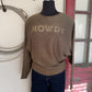 Brown sweater with 'HOWDY' text on a mannequin against a neutral wall.