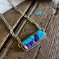 Necklace with a rectangular pendant featuring blue and purple stones on a wooden surface.