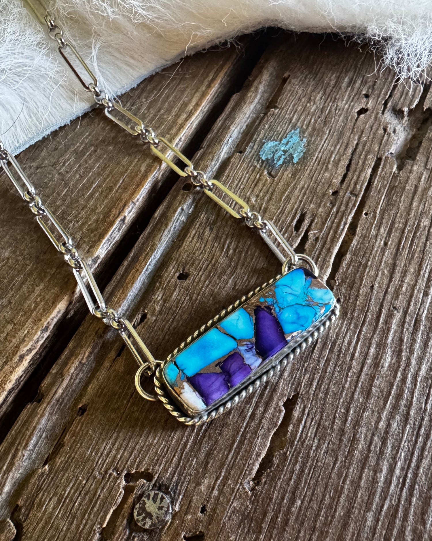 Necklace with a rectangular pendant featuring blue and purple stones on a wooden surface.