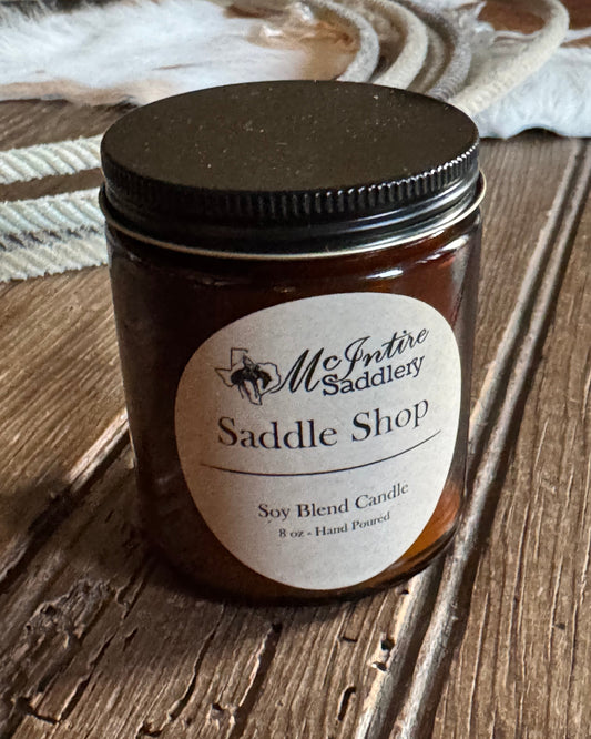 Jar of candle with 'Saddle Shop' label on a wooden surface