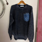Dark long sleeved shirt on a white surface with a wooden hanger and metal object.