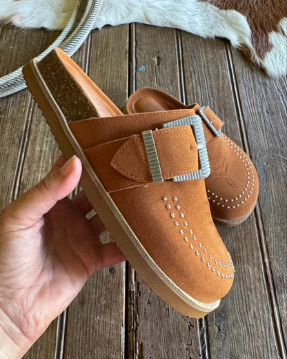 Brown leather shoe with a buckle held by a hand on a wooden surface
