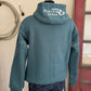 Blue hoodie with 'Ranch Girls' logo on a person standing against a wall with a red door and coiled rope.