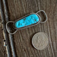 Turquoise stone pendant with silver wire wrapping on a wooden surface next to a coin for scale.