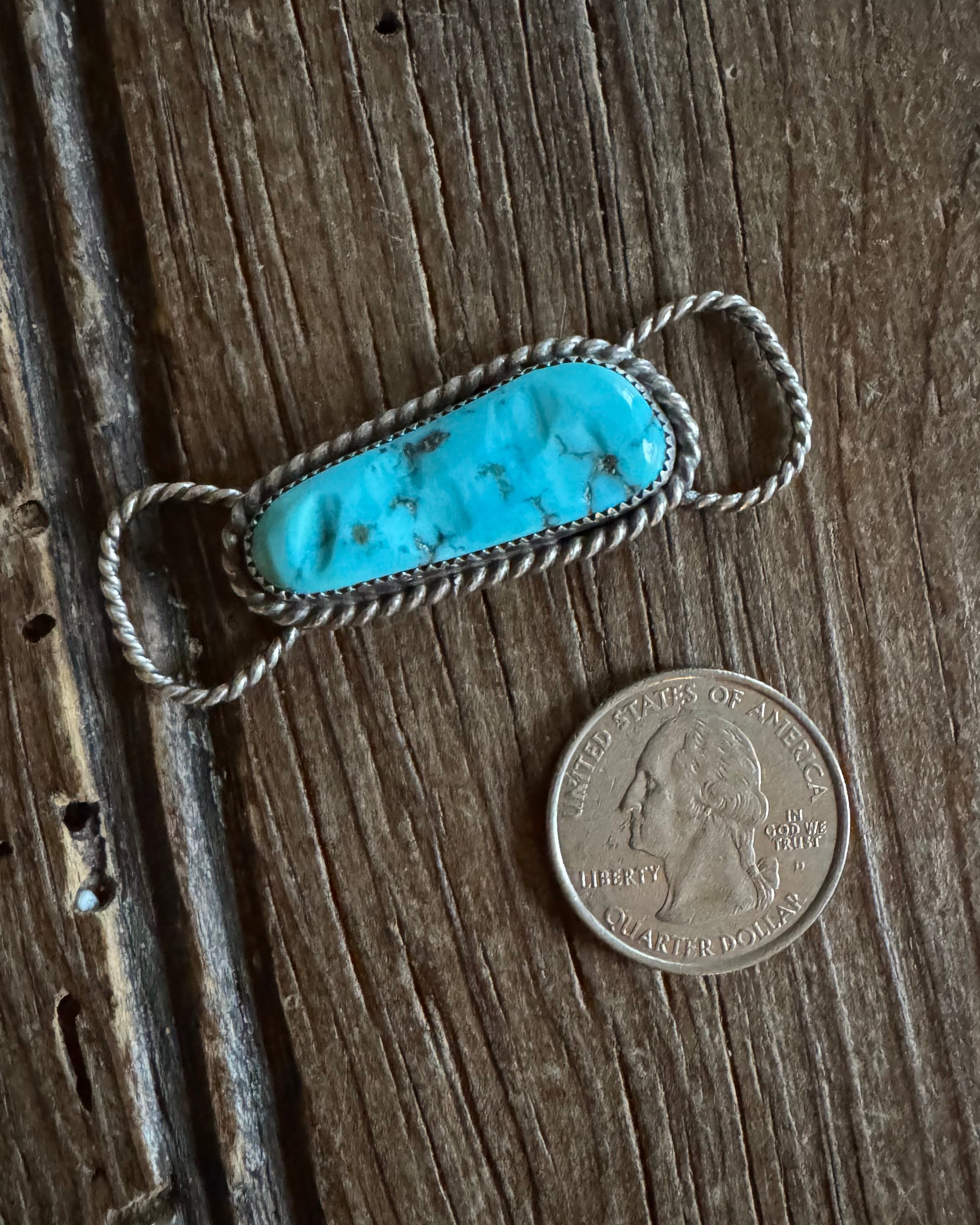 Turquoise stone pendant with silver wire wrapping on a wooden surface next to a coin for scale.