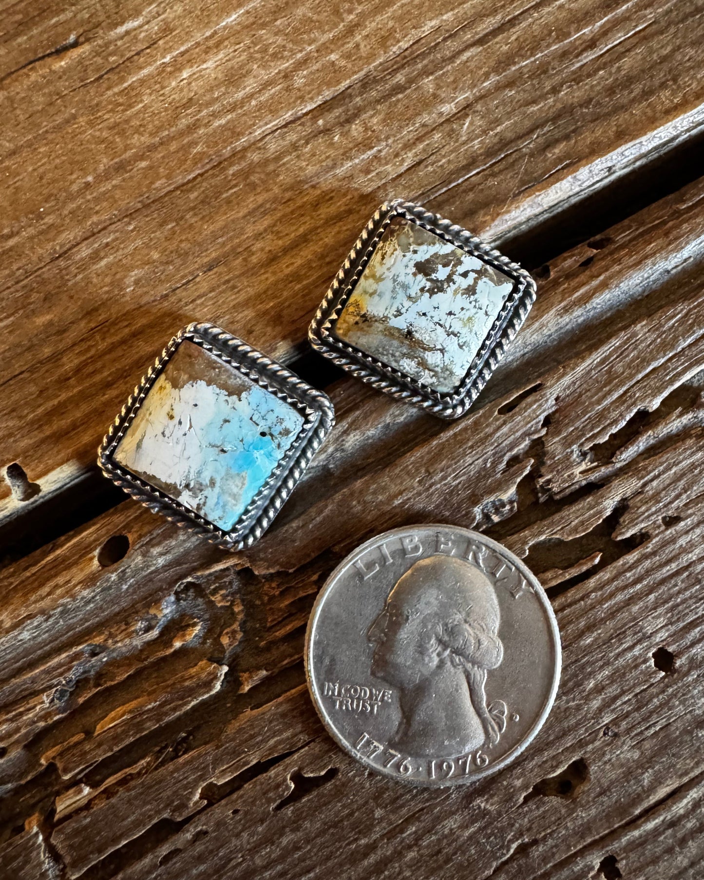 Pair of square earrings with a coin for scale on a wooden surface