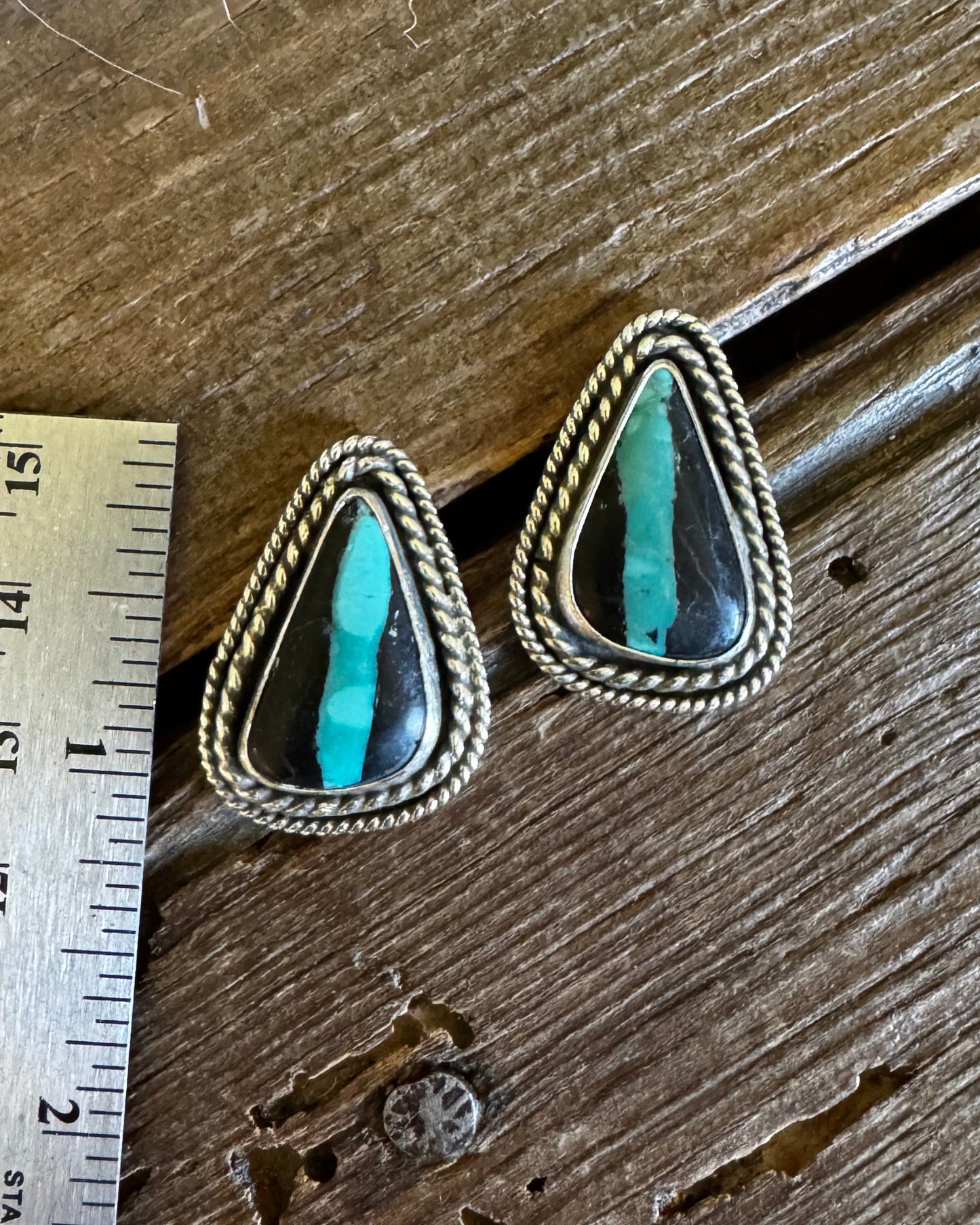 Pair of silver earrings with turquoise stones on a wooden surface with a ruler for scale.