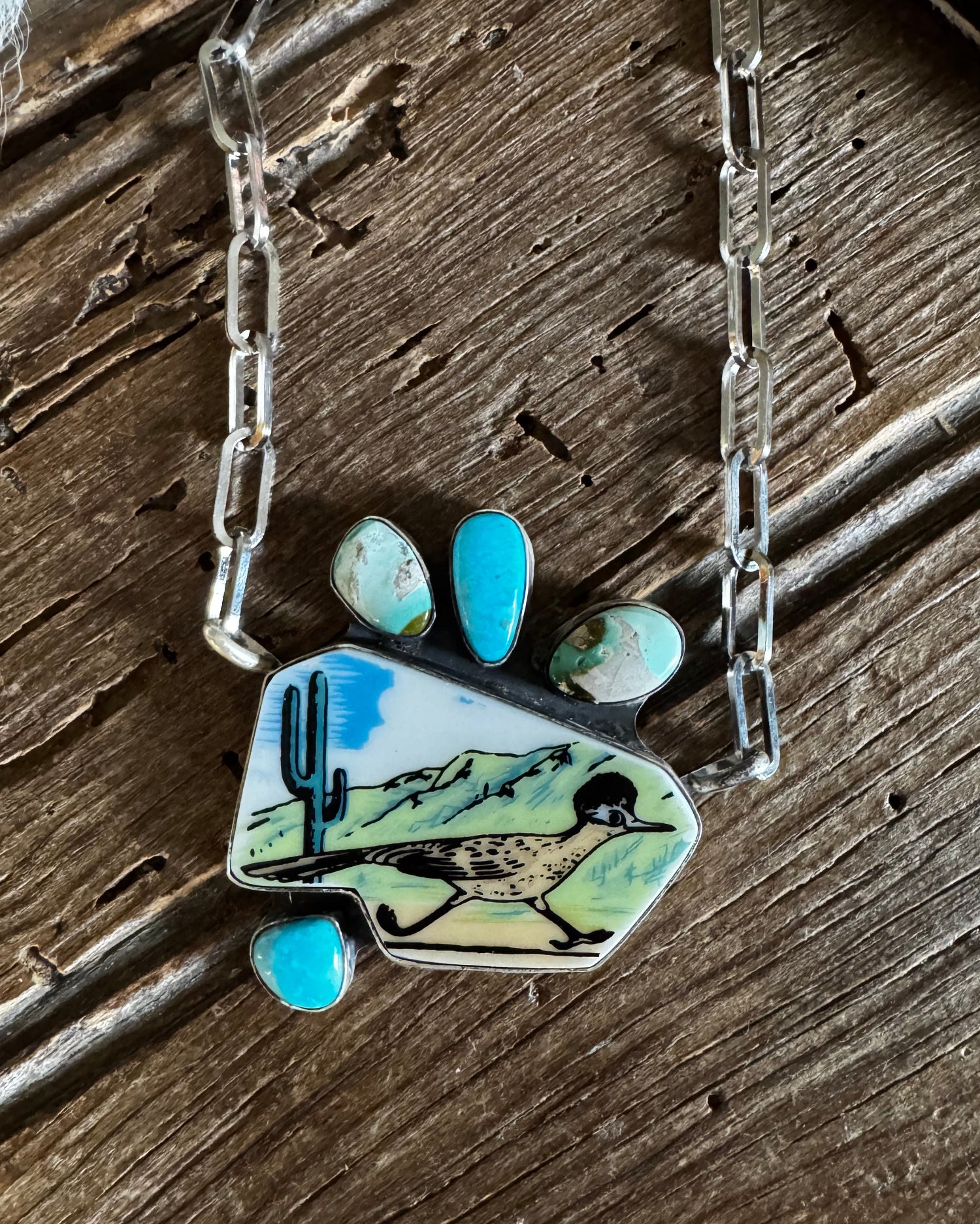 Necklace with a paw-shaped pendant featuring a bird design on a wooden surface