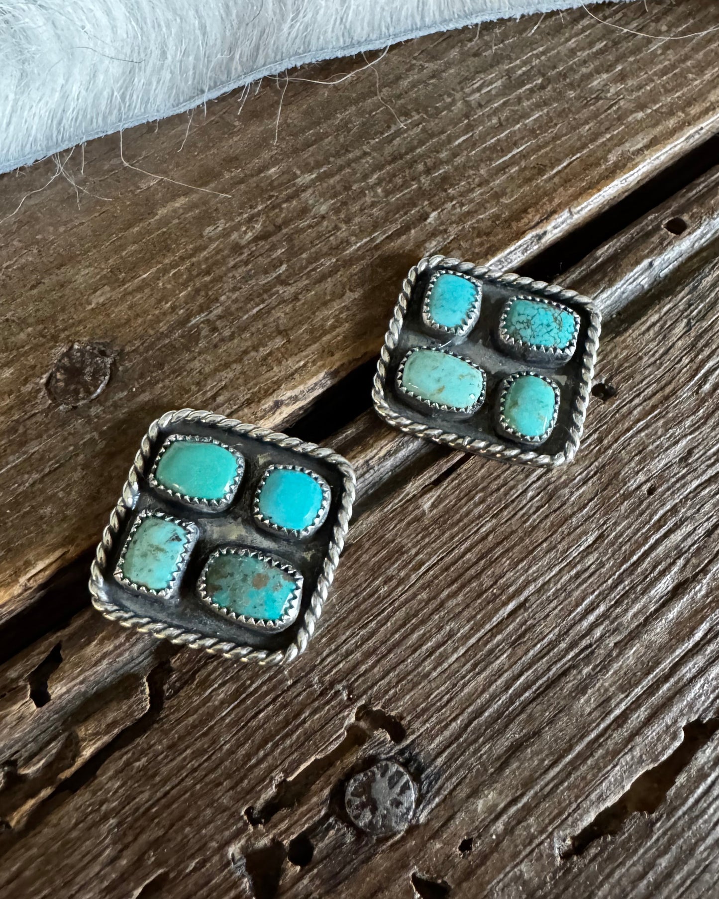Pair of square earrings with turquoise stones on a wooden surface