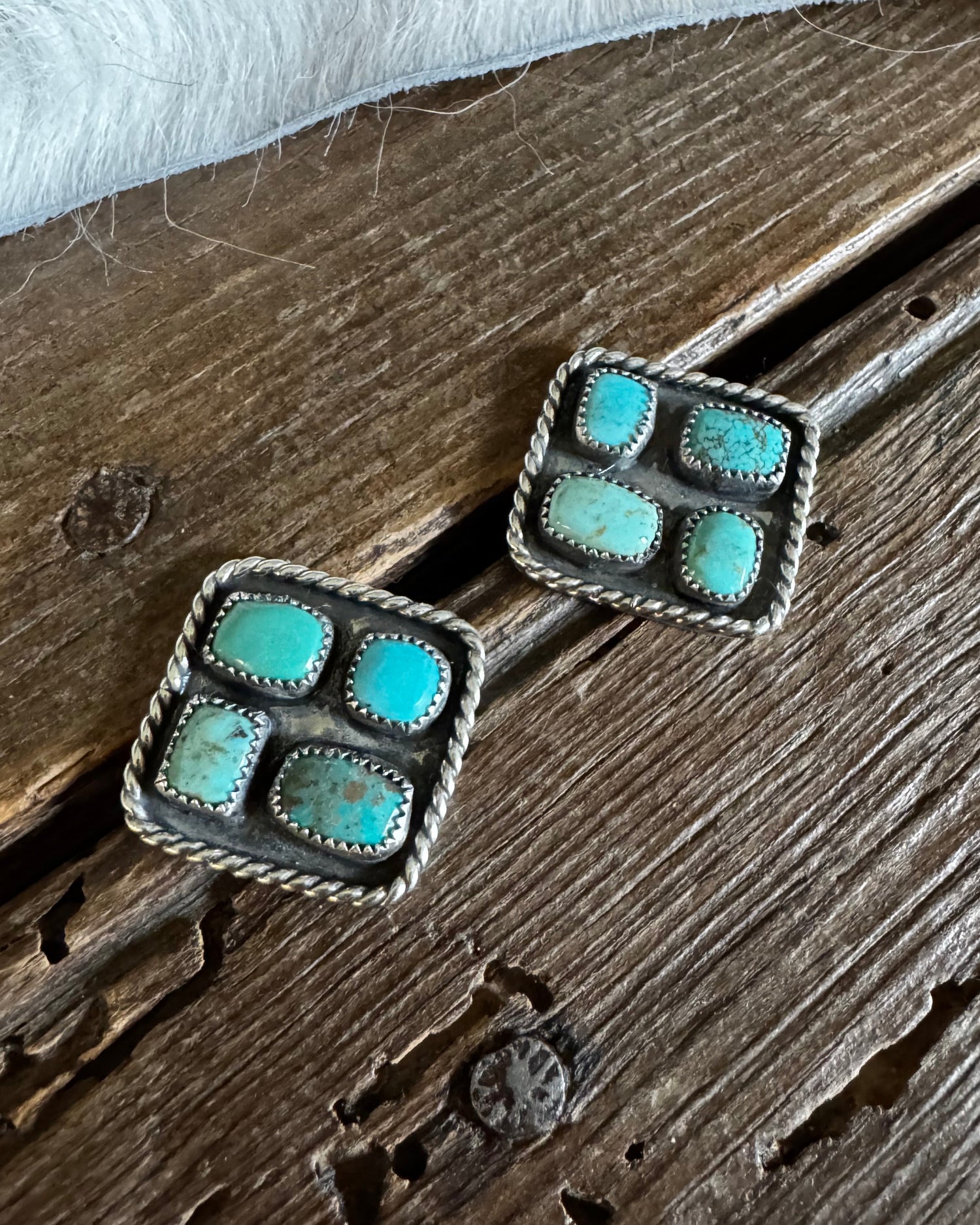 Pair of square earrings with turquoise stones on a wooden surface