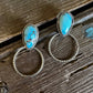 Turquoise stone earrings on a wooden surface with white fur in the background