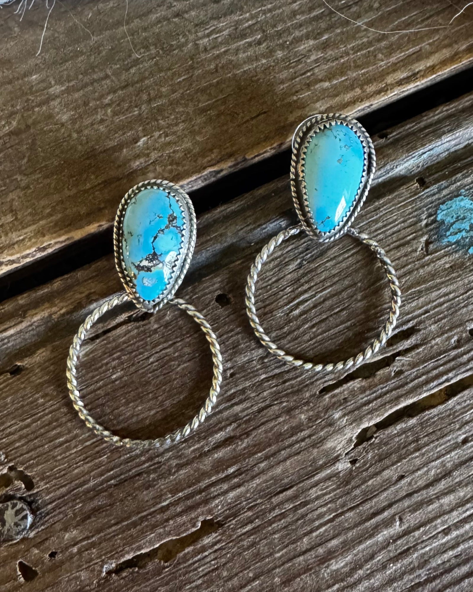 Turquoise stone earrings on a wooden surface with white fur in the background