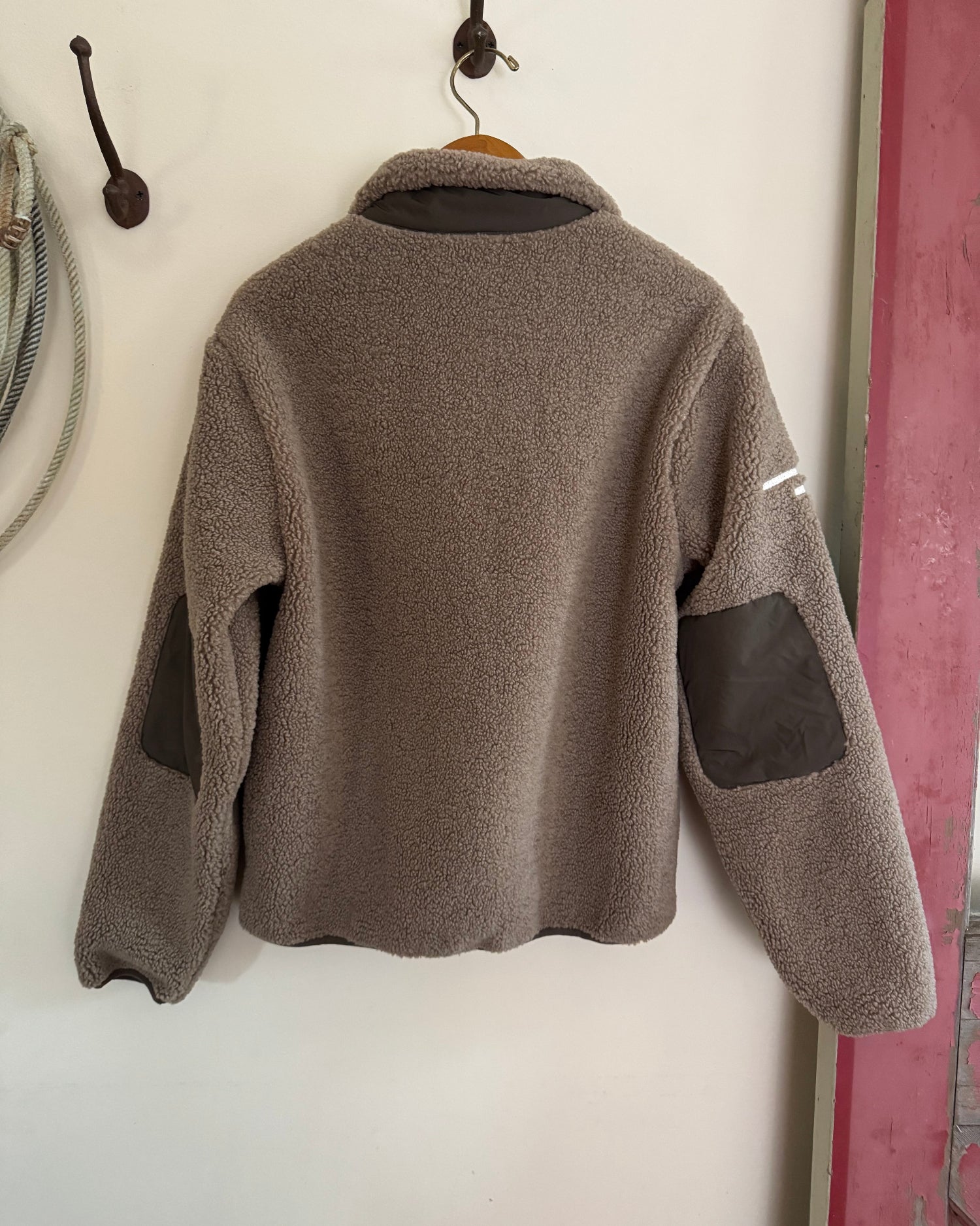 Gray fleece jacket with black patches hanging on a wall