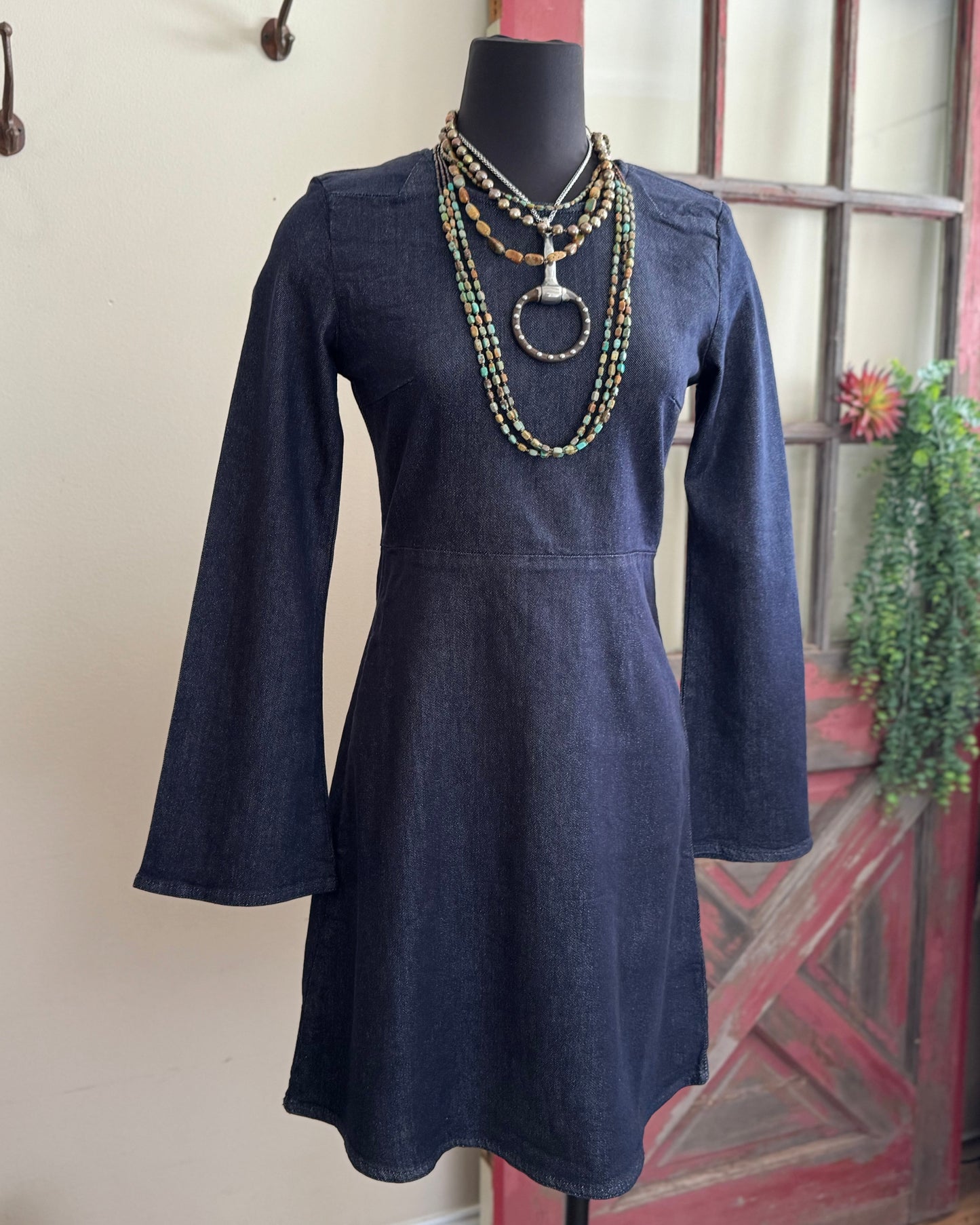 Navy blue dress on a mannequin with a necklace against a neutral wall.
