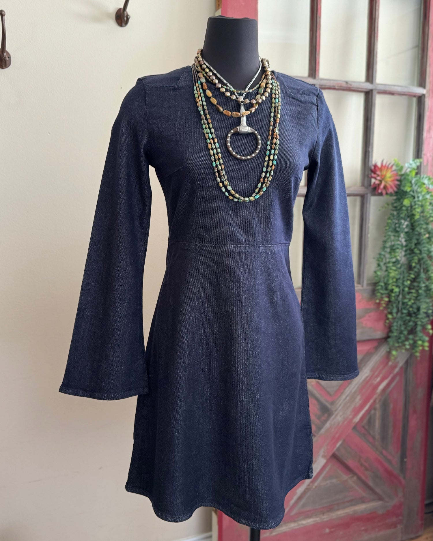 Navy blue dress on a mannequin with a necklace against a neutral wall.