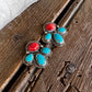 A pair of silver stud earrings with red and turquoise stones, displayed on a rustic wooden surface next to a white faux fur trim.