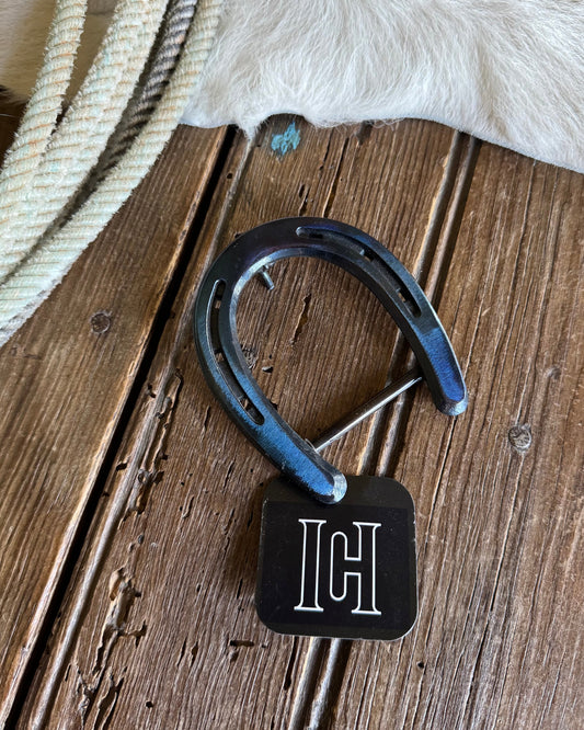 Horseshoe with a black tag featuring a white monogram on a wooden surface.