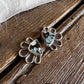 A pair of silver-toned stud earrings with a teardrop-shaped turquoise and black inlay, displayed on a rustic wooden surface next to white faux fur.