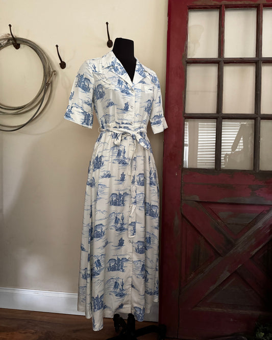 White dress with blue patterns on a mannequin against a rustic background with a red door and wooden wall.