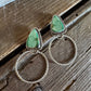 A pair of handmade silver dangle earrings with triangular green stone tops and large twisted hoop drops, displayed on a rustic wooden surface.