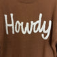 Brown sweater with white 'Howdy' text on a close-up view