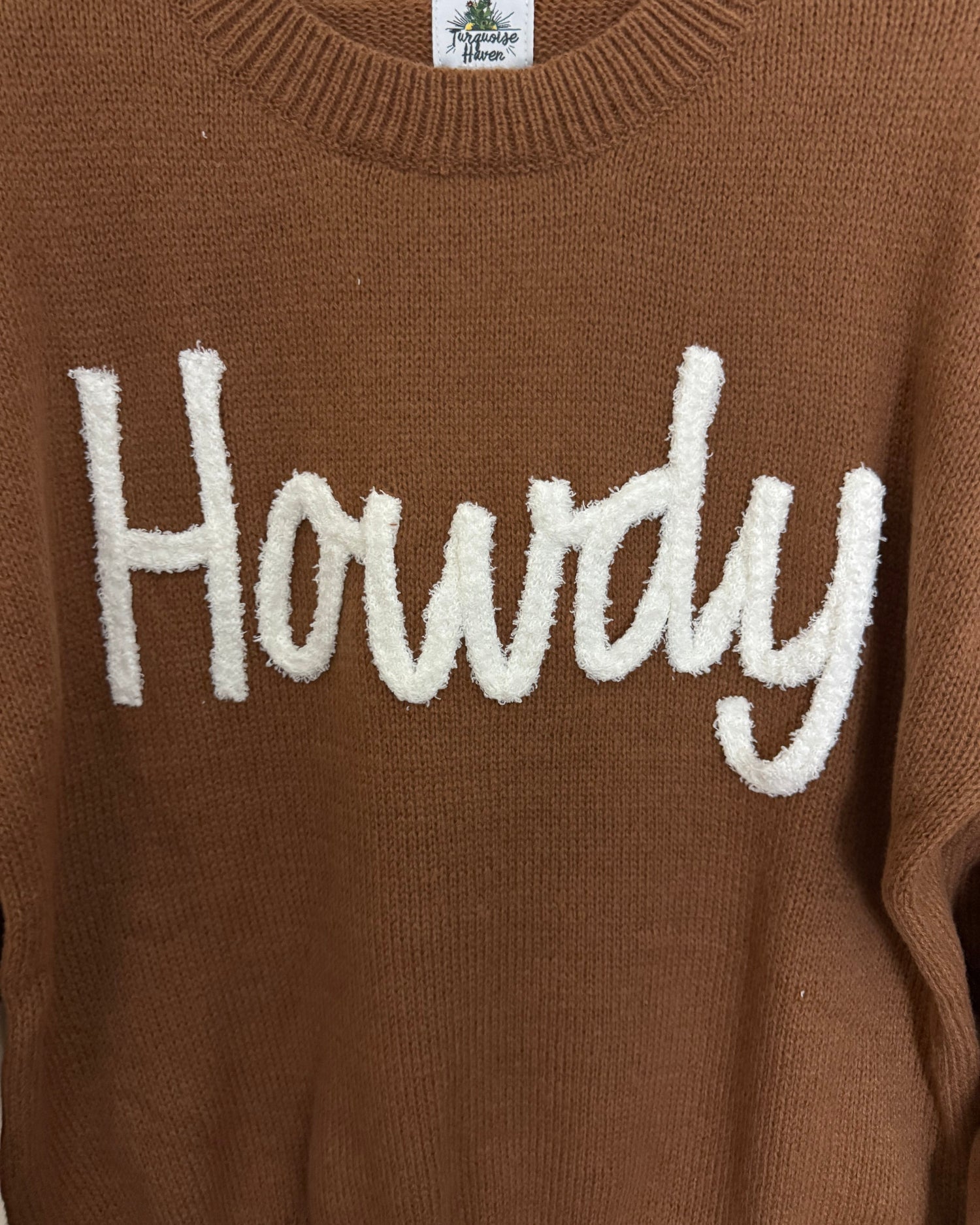Brown sweater with white 'Howdy' text on a close-up view