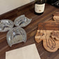 Three silver wine coasters on a wooden surface with a bottle of Meiomi wine and a wooden cutting board.