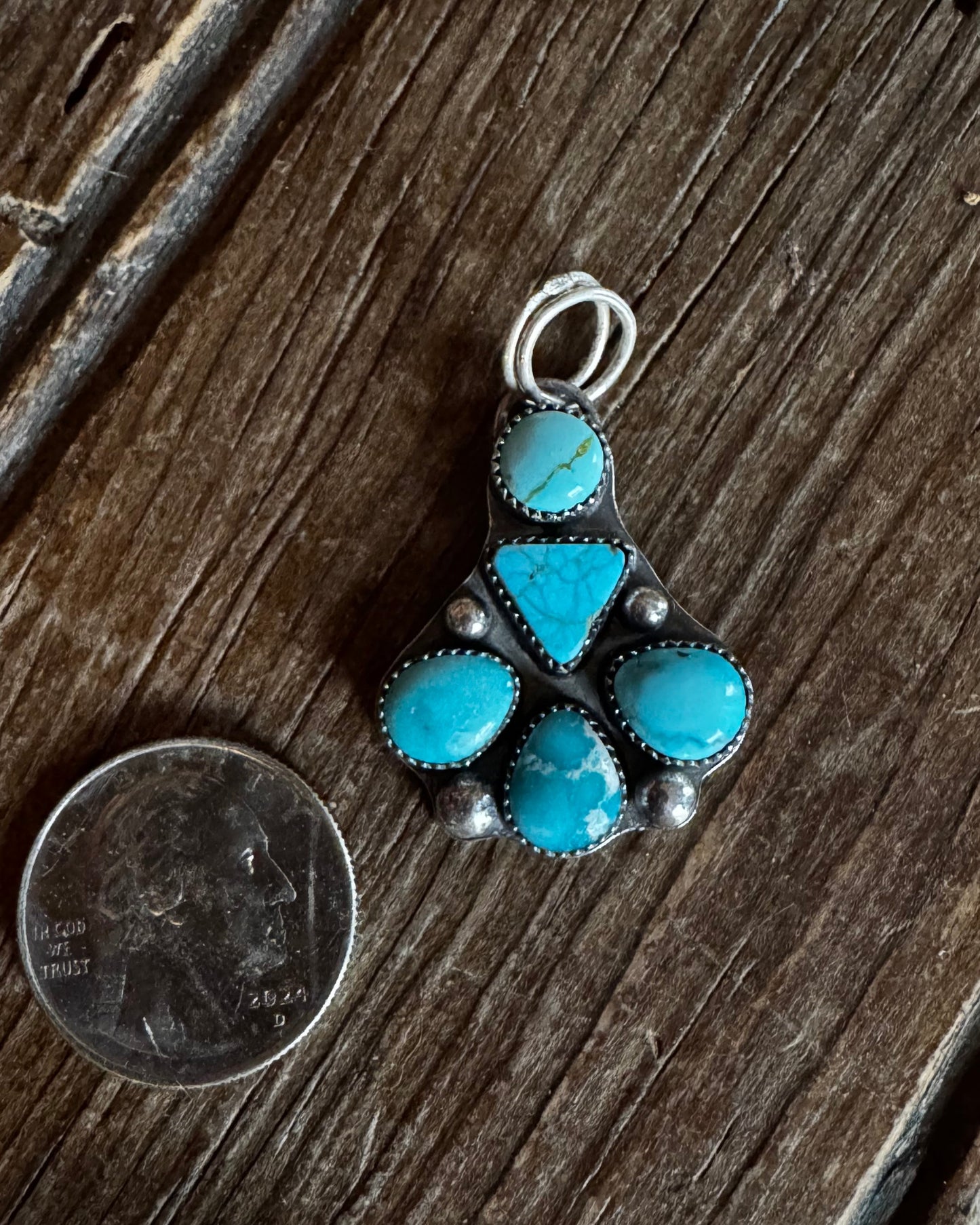 Turquoise stone pendant on a wooden surface with a coin for scale
