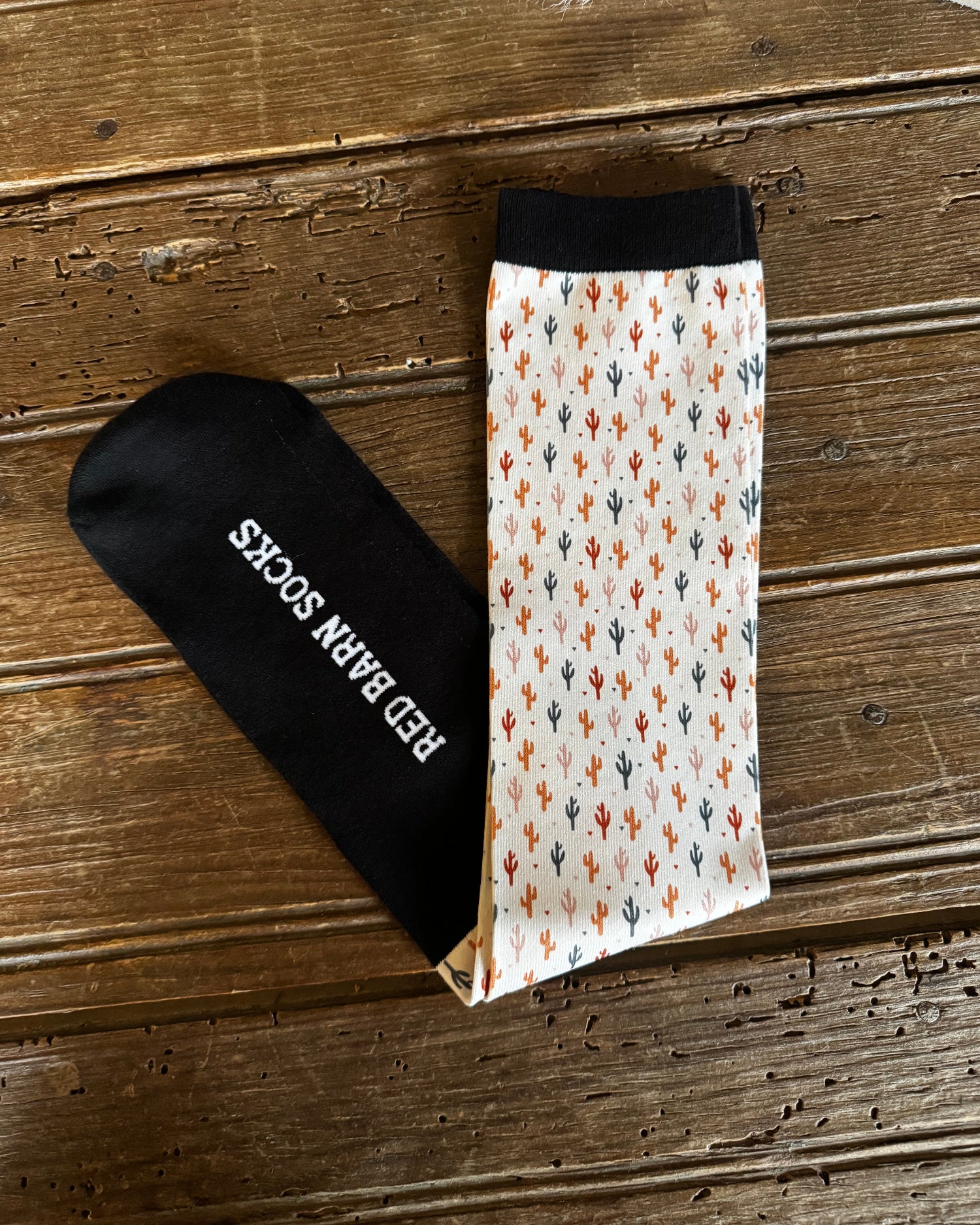 Two pairs of socks, one black and one with cactus pattern, on a wooden surface.