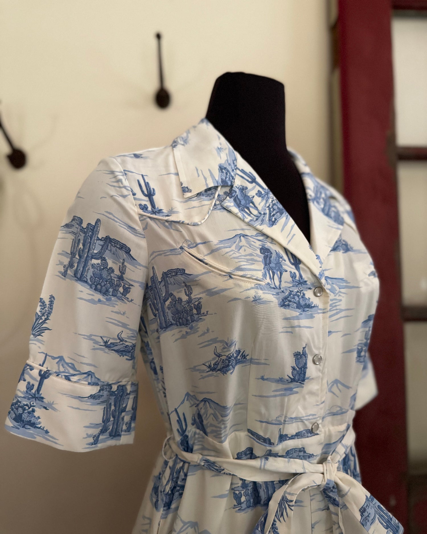 White dress with blue pattern on a mannequin against a neutral background