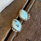 A pair of turquoise statement earrings with gold settings, displayed on a rustic wooden surface next to a white fur trim.