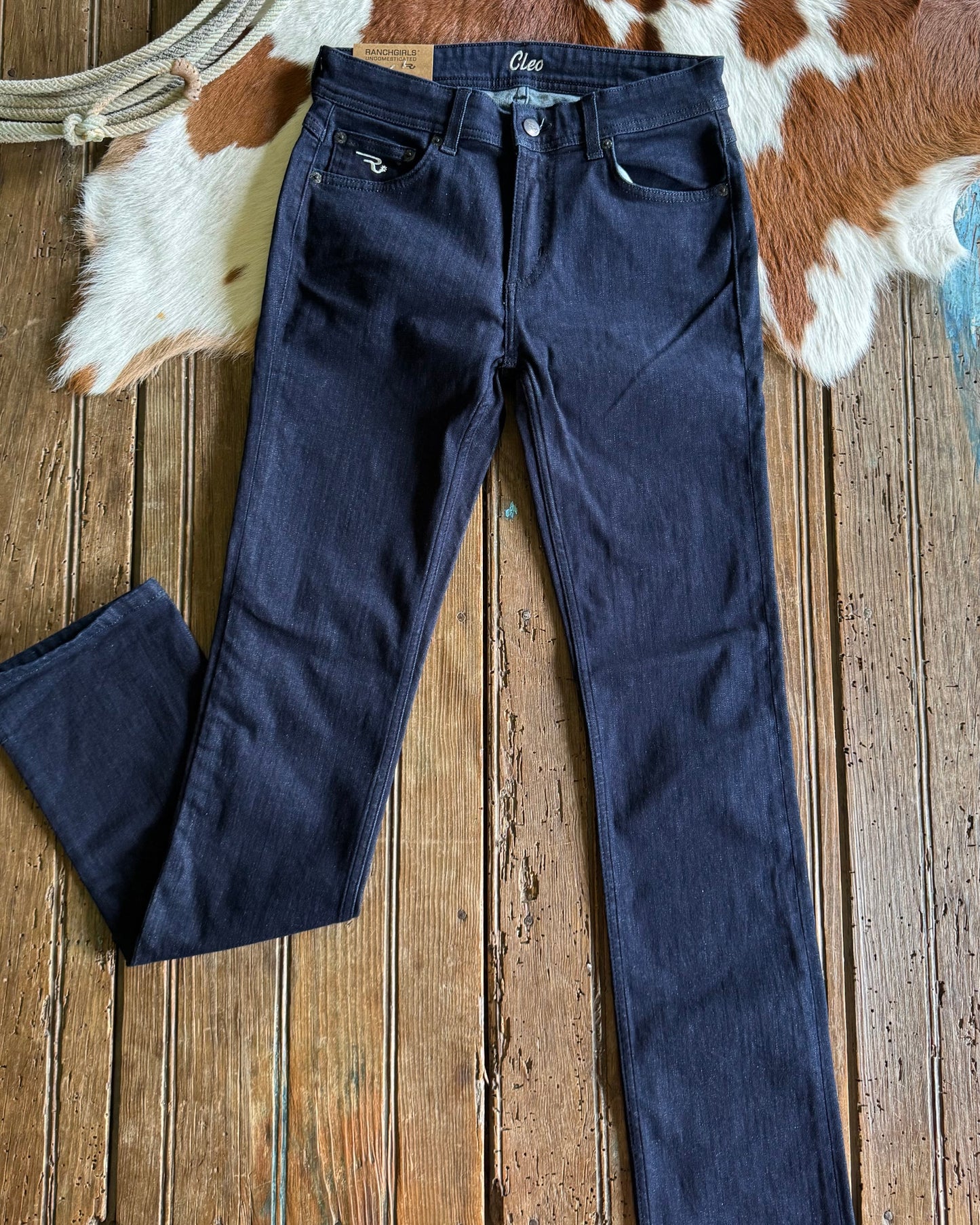 Dark blue jeans on a wooden surface with a cowhide rug in the background