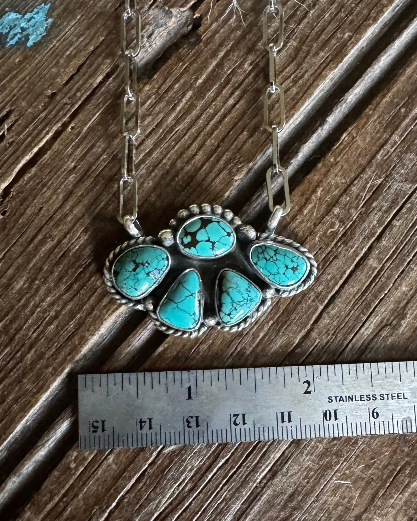 Turquoise pendant necklace on a wooden surface with a ruler for scale.
